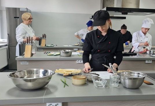 Uczestnicy bloku „gastronomia” w eliminacjach praktycznych i Pani Profesor Iwona Adamska oceniająca umiejętności wykonania przez nich naleśników. 