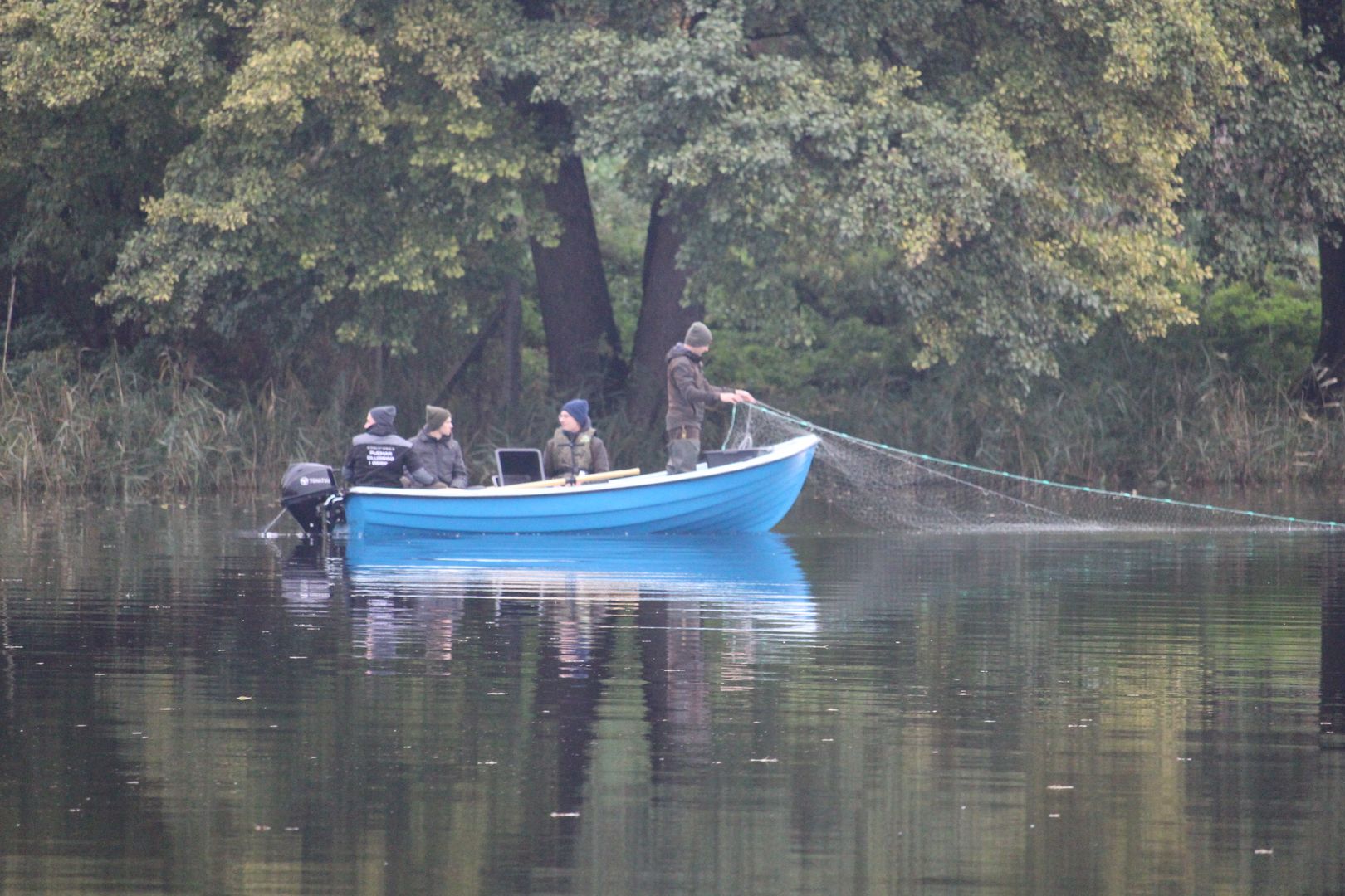 Studencji na łodzi spalinowej wyciągają sieci z jeziora.