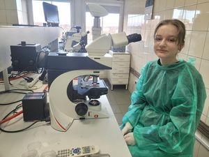 Uczeń w zielonym fartuchu laboratoryjnym siedzi przy mikroskopie.